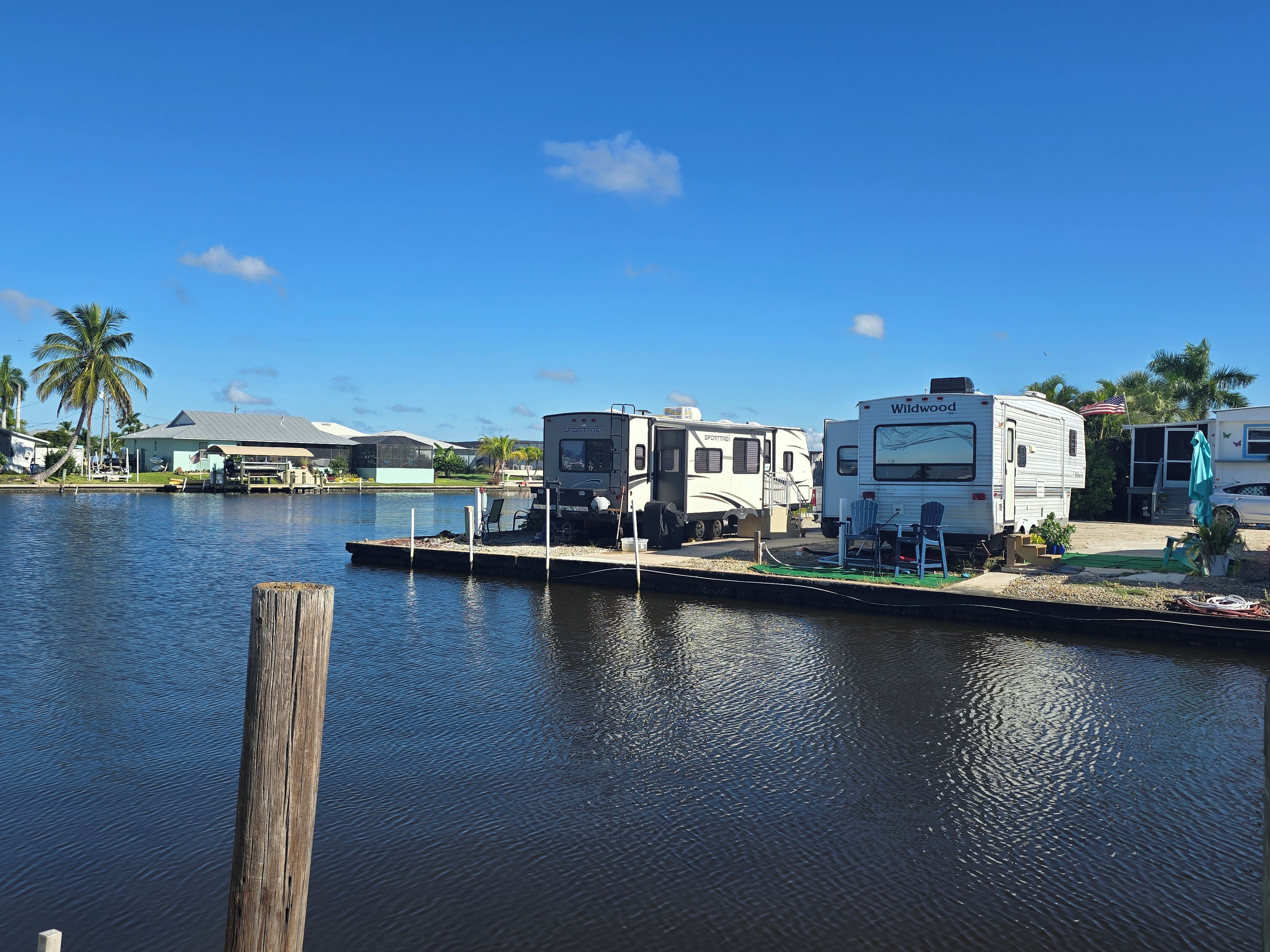 A marina with RVs docked, calm water, and a clear sky.