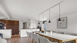 Una cucina moderna con mobili in legno, un piano di lavoro bianco e una zona pranzo con un tavolo lungo e sedie.