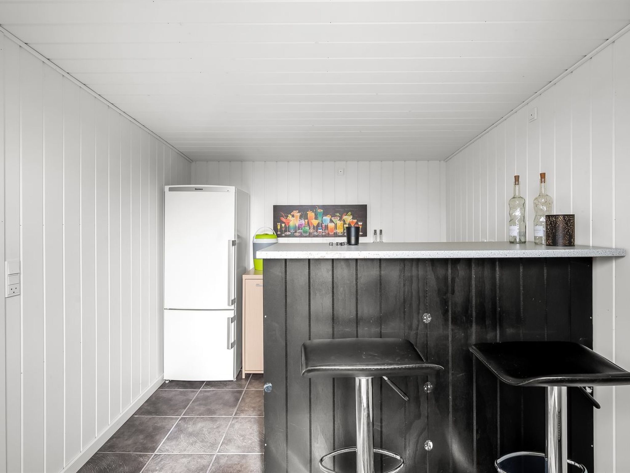 A compact kitchen with a white refrigerator, a bar counter, and two stools.
