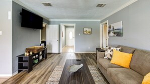 A living room with a sofa, a coffee table, a TV mounted on the wall, and a hallway leading to another room. - Private Pool Paradise in La Porte. Family & Work Stays Welcome (La Porte)