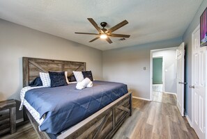 Un dormitorio con cama, cabecera de madera, ventilador de techo y una puerta que da a otra habitación.