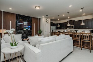 Ein modernes Wohnzimmer mit Sofa, Esstisch und Küchenzeile mit Schränken und Geräten.