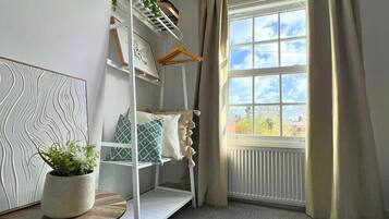 A room with a bunk bed, a radiator, a window with curtains, a plant on a table, and a wall with a textured design.