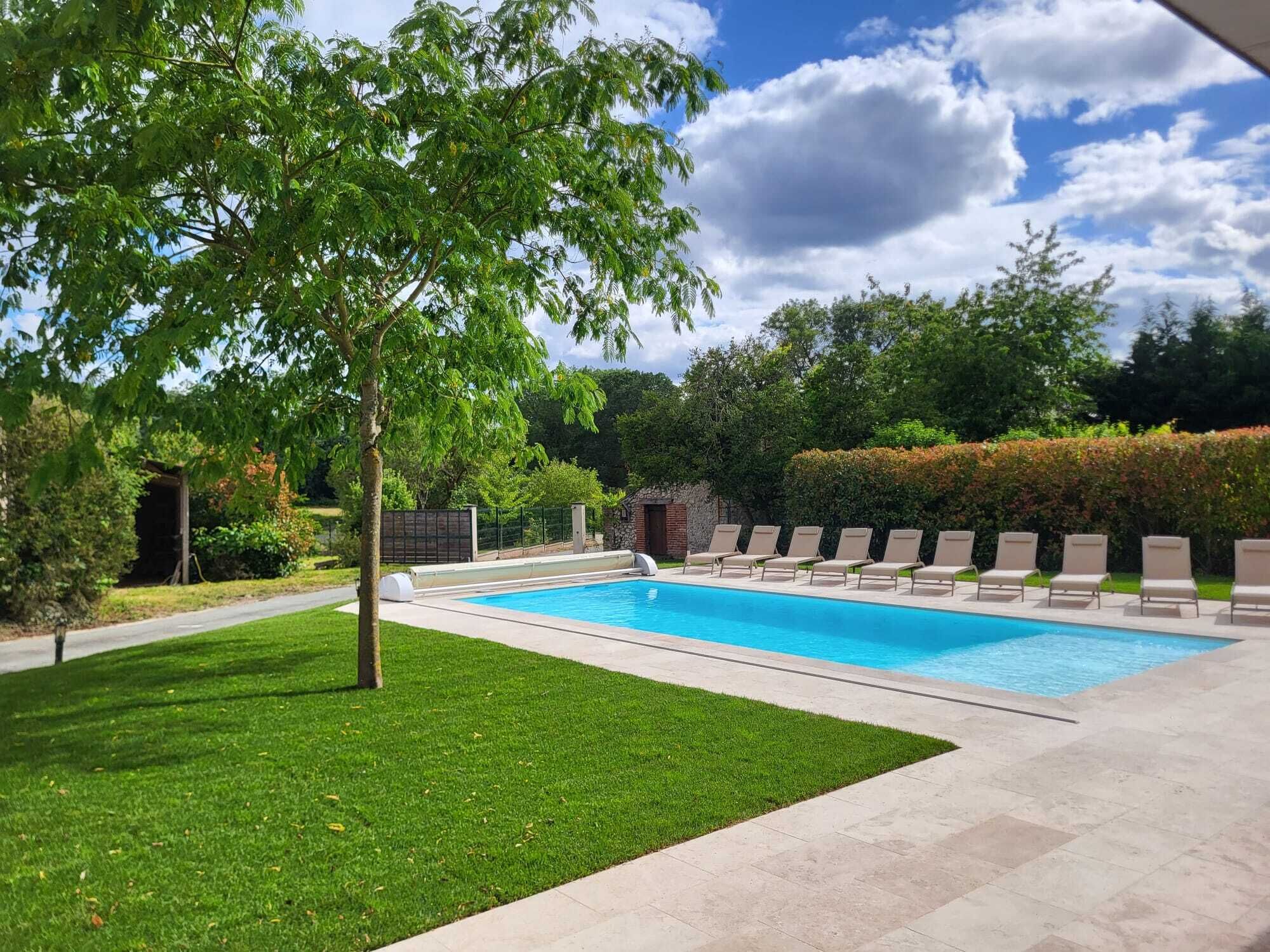 A rectangular swimming pool with a tiled deck, surrounded by a well-maintained lawn and a hedge.