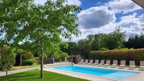 Una piscina rectangular amb una zona enrajolada al voltant, envoltada per un pràt ben cuidat i una tanca.