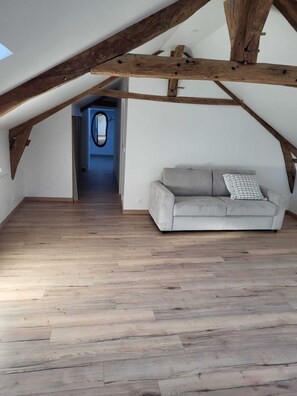 Ein Dachzimmer mit Holzbalken, einer Couch und einem Gang zu einem weiteren Raum.