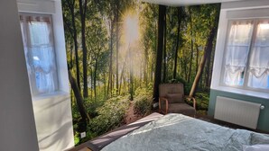 Un dormitori amb un llit, una cadira i un mural gran amb un bosc a la paret.