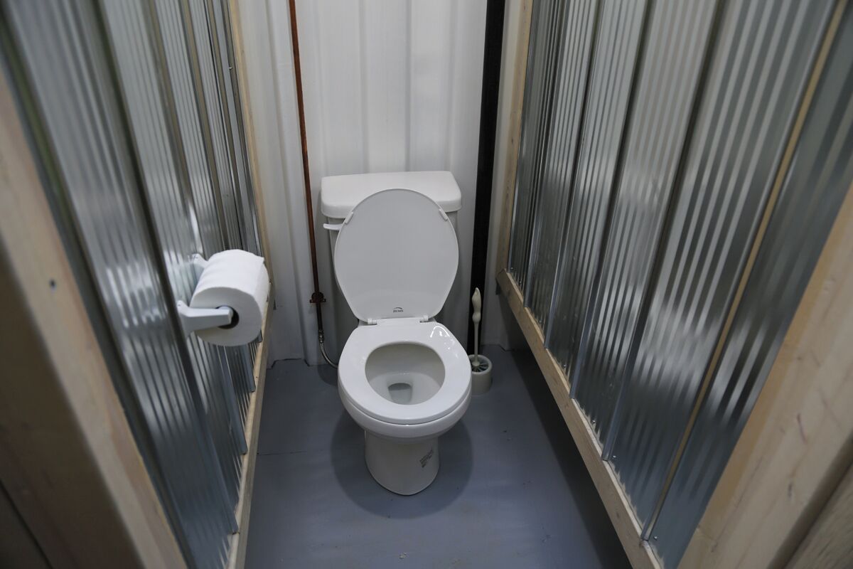 Ein schmales Badezimmer mit Toilette, Toilettenpapierhalter und einer Toilettenpapierrolle auf dem Boden.