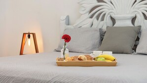 Ein ordentlich bezogenes Bett mit einem Tablett Gebäck, einer Banane und einer roten Blume.