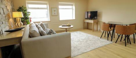 A modern living room with a sofa, a dining table with chairs, a TV, and a lamp.
