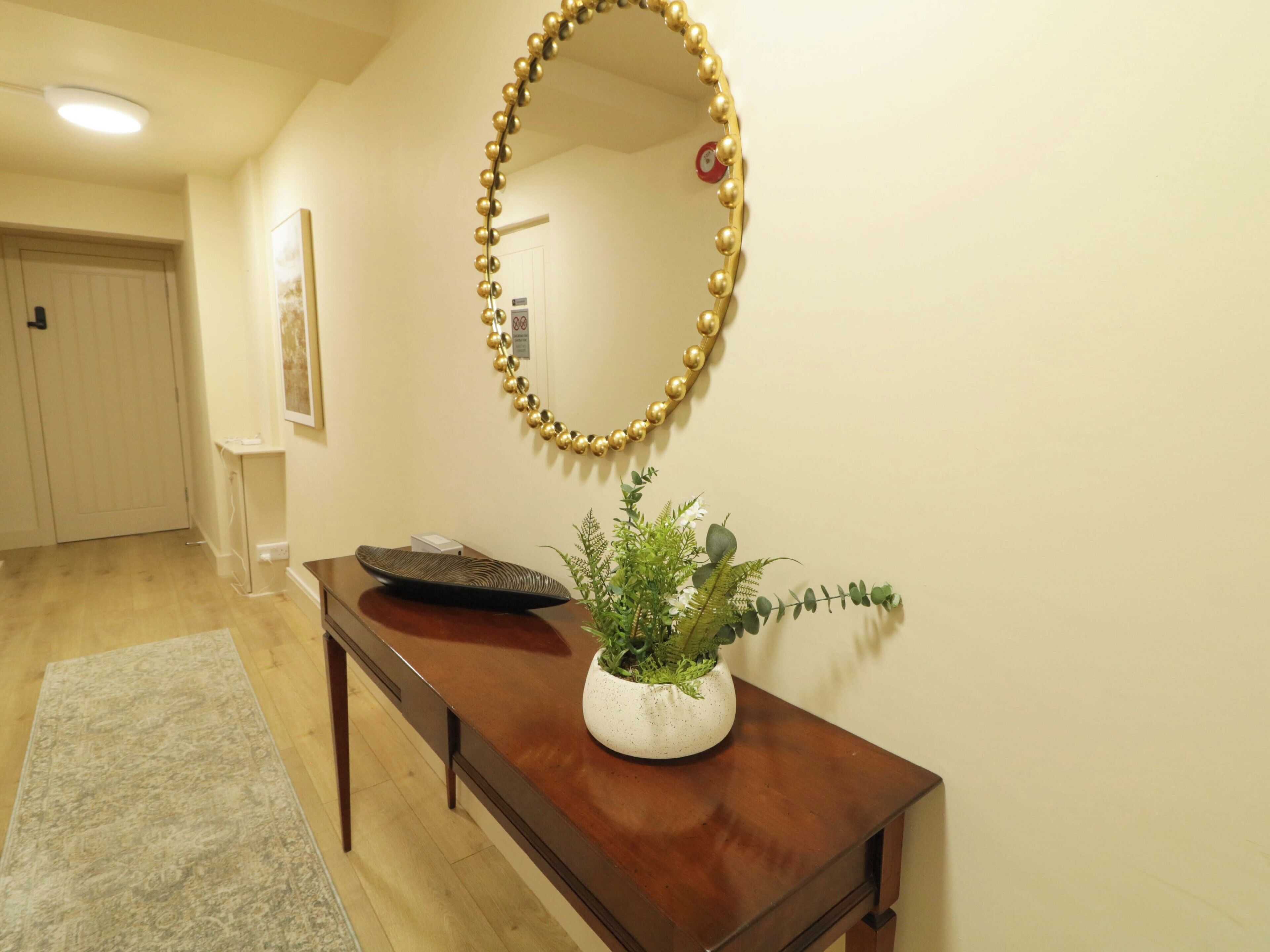 A hallway with a wooden bench, a potted plant, and a wall-mounted mirror.