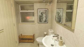 A bathroom with a toilet, sink, mirror, framed picture, and a window with frosted glass.