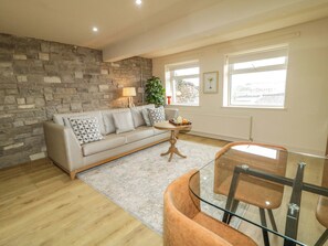 A living room with a stone wall, a sofa, a glass table, and a view through the windows. - Suite 33A (Londonderry)