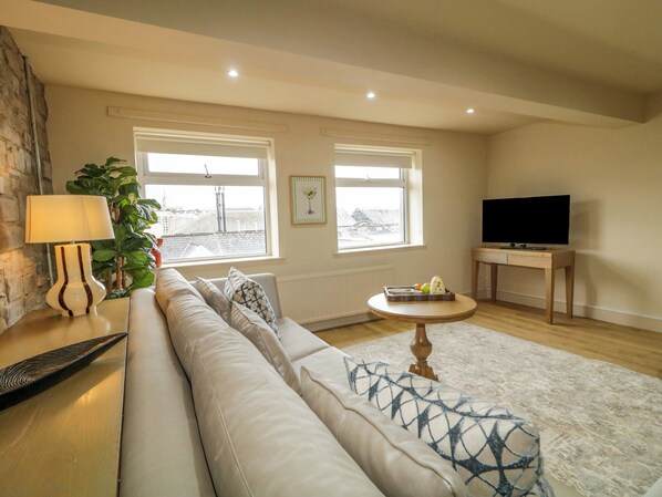 A living room with a sofa, a lamp, a TV, and a window with a view. - Suite 33A (Londonderry)