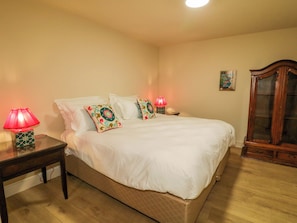 A bedroom with a bed, two bedside tables, a nightstand, a wooden cabinet, and a wall-mounted picture. - Suite 33A (Londonderry)