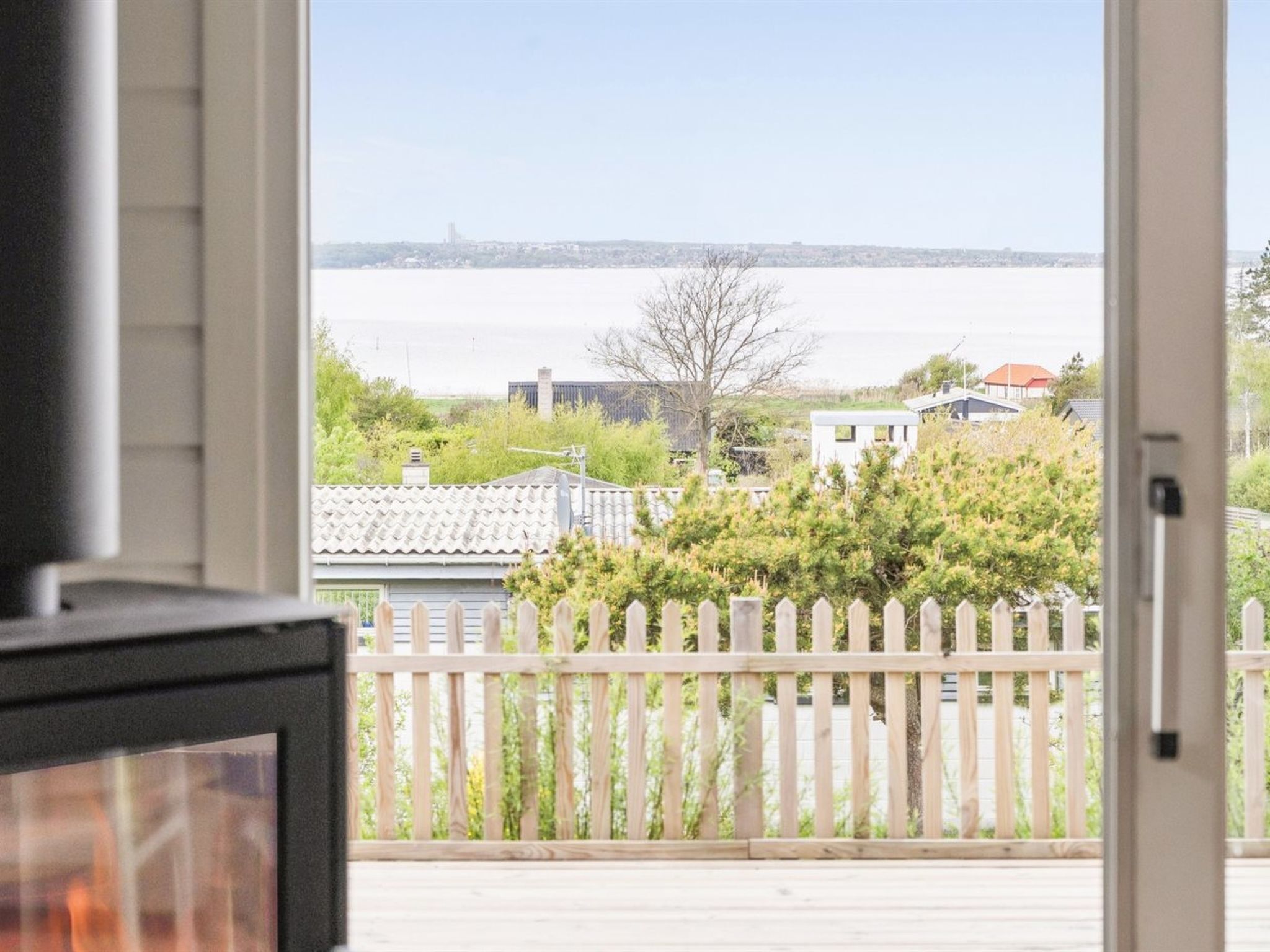 A view from a window overlooking a residential area with a wooden fence, houses, and a body of water in the distance.