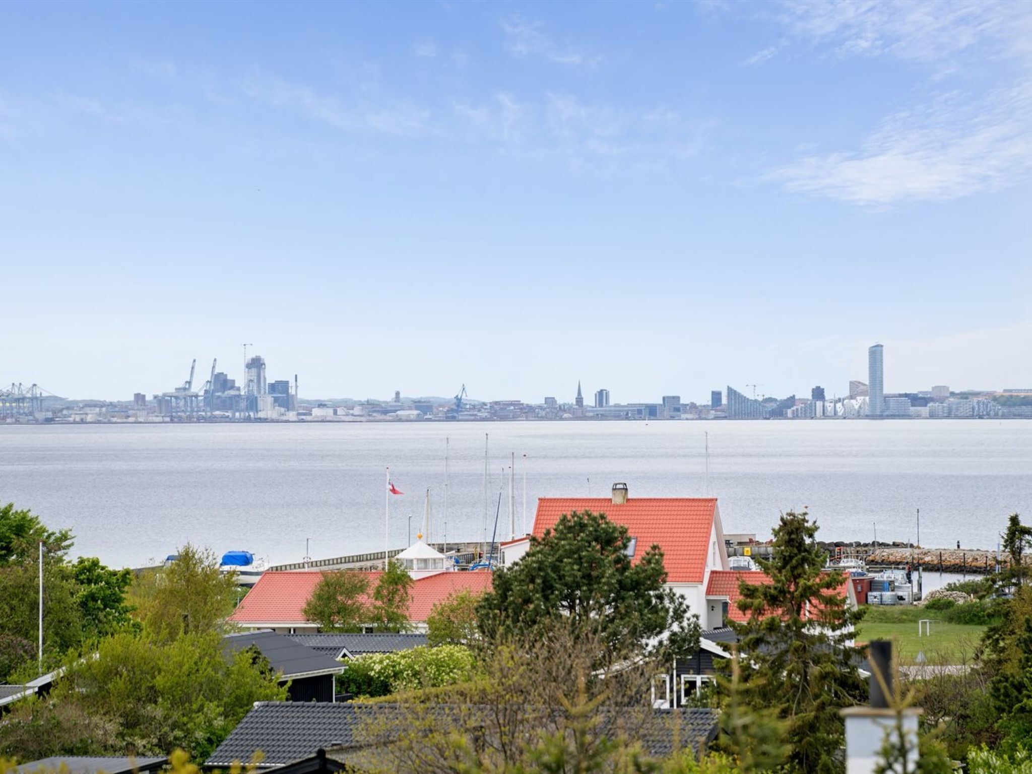A coastal cityscape with a large body of water, a red-roofed building, and a distant skyline.