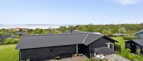 A black building with a sloped roof, a covered outdoor seating area, and a view of a body of water in the background.