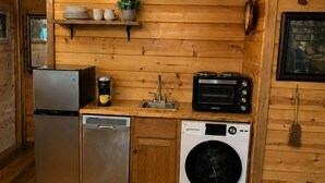 A compact kitchen with wooden walls, a refrigerator, dishwasher, microwave, sink, and hanging light fixtures.