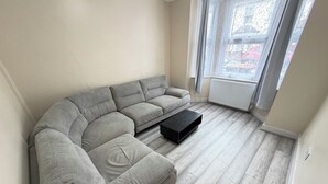 Ein Wohnzimmer mit einem grauen Ecksofa, einem schwarzen Couchtisch und einem Fenster mit Vorhängen.