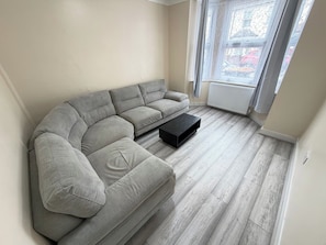 Ein modernes Wohnzimmer mit einem grauen Ecksofa, einem schwarzen Couchtisch und hellem Holzboden.