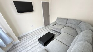 Ein Wohnzimmer mit Ecksofa, flachbildfernseher an der Wand und einer Tür.