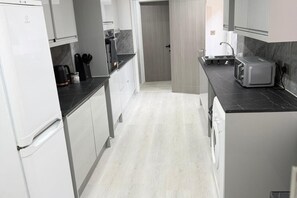 A modern kitchen with white cabinetry, a built-in oven, a microwave, and a toaster on the countertop. - 3 Bed House Long Stays Fast Wi-fi & Parking (Bedford)