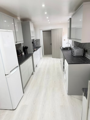 A modern kitchen with white appliances, a black countertop, and a grey floor.