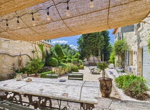 Patio esterno con tavolo e sedie, circondato da muri in pietra e vegetazione.