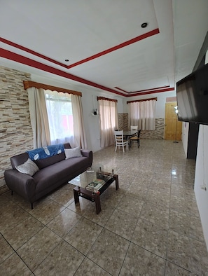 A living room with a sofa, coffee table, dining table, and chairs. - Volcano View Tropical Farmhouse! Private Farm Stay; AC near La Fortuna Waterfall (La Fortuna)