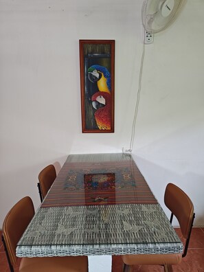 A dining table with a woven tablecloth, four chairs, and a framed painting of parrots on the wall. - Volcano View Tropical Farmhouse! Private Farm Stay; AC near La Fortuna Waterfall (La Fortuna)