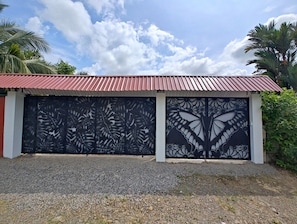A gated entrance with decorative metalwork, a red roof, and gravel ground. - Volcano View Tropical Farmhouse! Private Farm Stay; AC near La Fortuna Waterfall (La Fortuna)