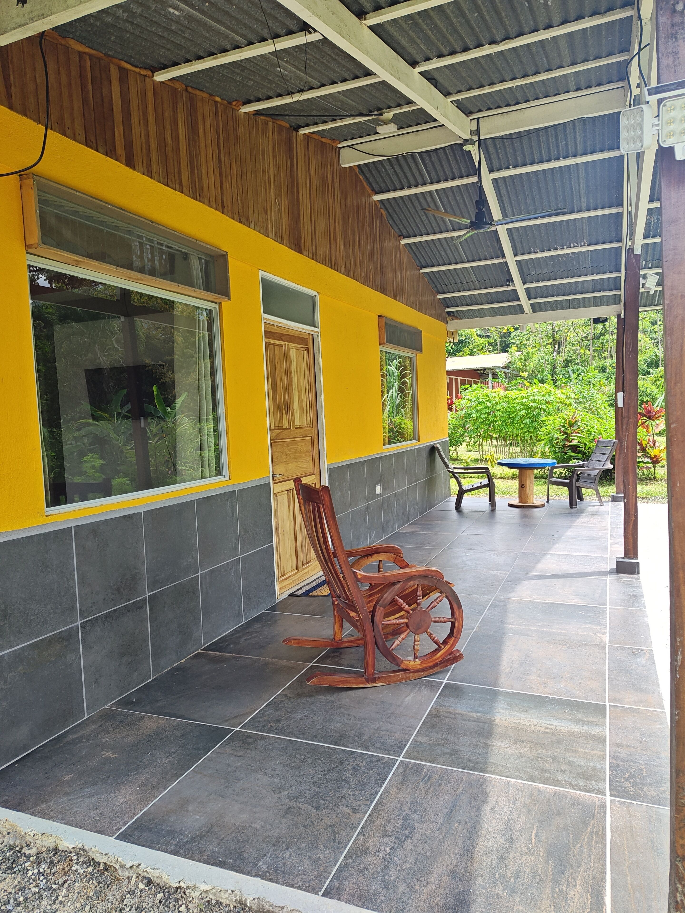 Un bâtiment à la façade jaune, doté d’un patio couvert avec une chaise berçante et d’un sol carrelé.