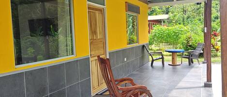 Un bâtiment à la façade jaune, doté d’un patio couvert avec une chaise berçante et d’un sol carrelé.