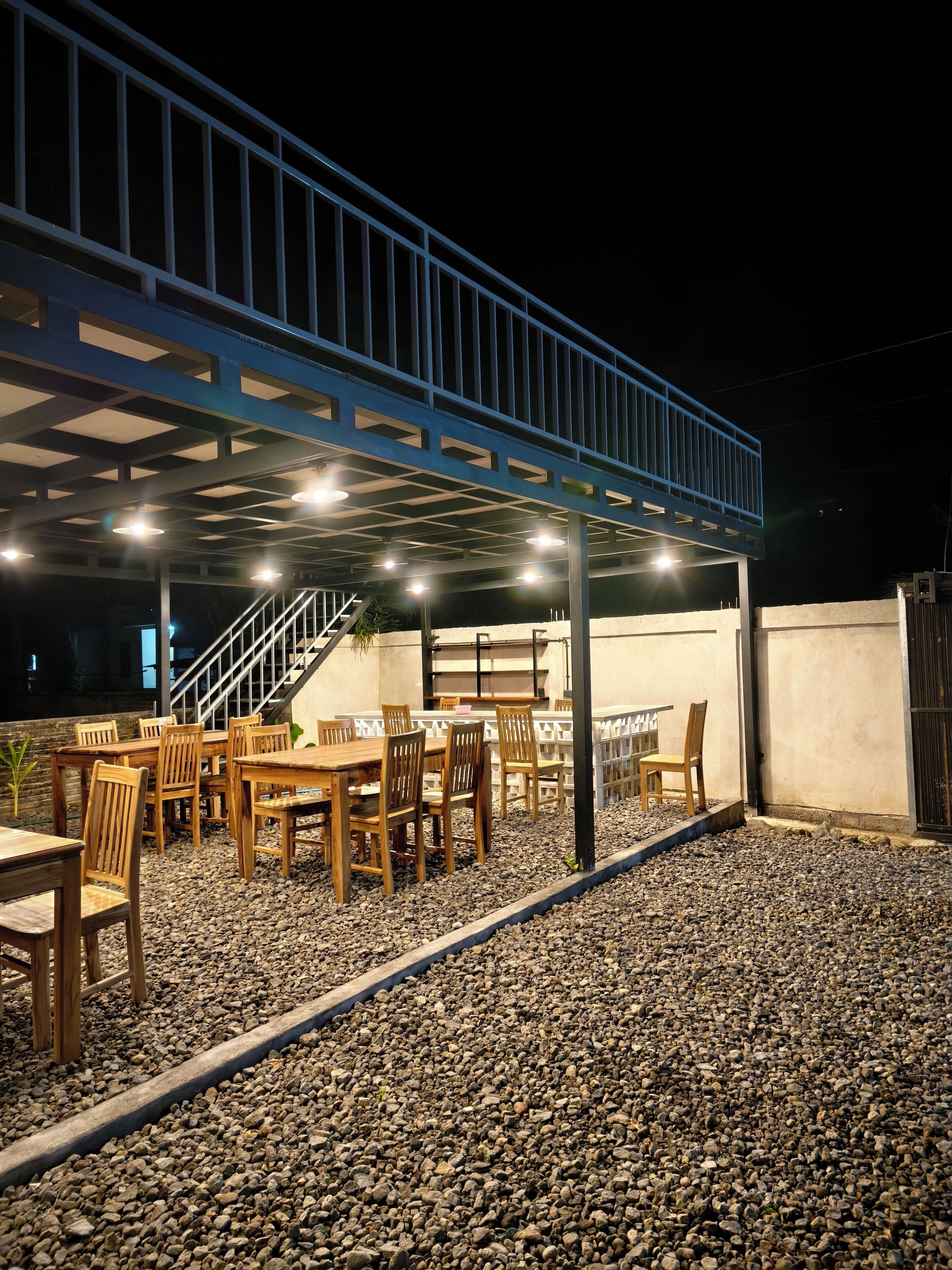 An outdoor seating area with tables and chairs, a covered section with railings, and a staircase leading to an upper level.
