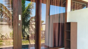 Una habitación con piso de mármol, puerta de madera y vista a un jardín con palmeras.