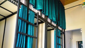 Habitación con literas, cortinas azul verdosas, una escalera y suelo de baldosas.