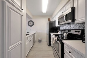 A narrow kitchen with white cabinetry, a microwave, a stove, and a clock on the wall. - 2BR/2BA Scottsdale Condo with heated pool (Scottsdale)