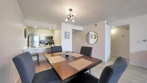 Eine moderne Küche mit weißen Schränken, einem Edelstahl-Kühlschrank und einer Mikrowelle. Es gibt einen Essbereich mit einem Holztisch und vier grauen Stühlen.