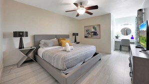 Ein Schlafzimmer mit Bett, Nachttischen, Deckenventilator, Schreibtisch und Fernseher.