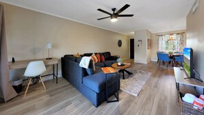 Ein modernes Wohnzimmer mit Sofa, Schreibtisch, Essbereich und Deckenventilator.