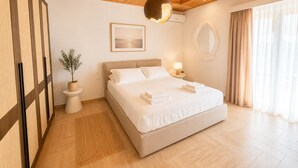 Habitación de hotel moderna con techo de madera, una cama grande, una mesita de noche con lámpara, una planta en maceta y vistas al exterior a través de grandes ventanales.
