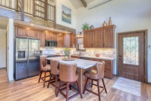 A kitchen with a central island, wooden cabinets, stainless steel appliances, and a dining area with leather chairs. - The Gold Hill Chalet W/ Private Hot Tub (Keystone)