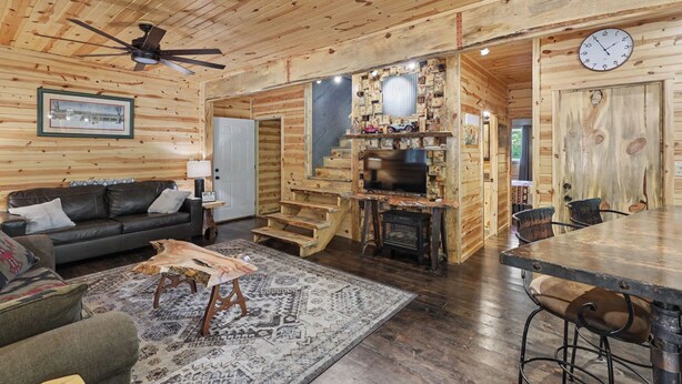 Un interior de madera con un sofá, una mesa de centro, una chimenea, un reloj y una escalera que conduce a otra habitación.