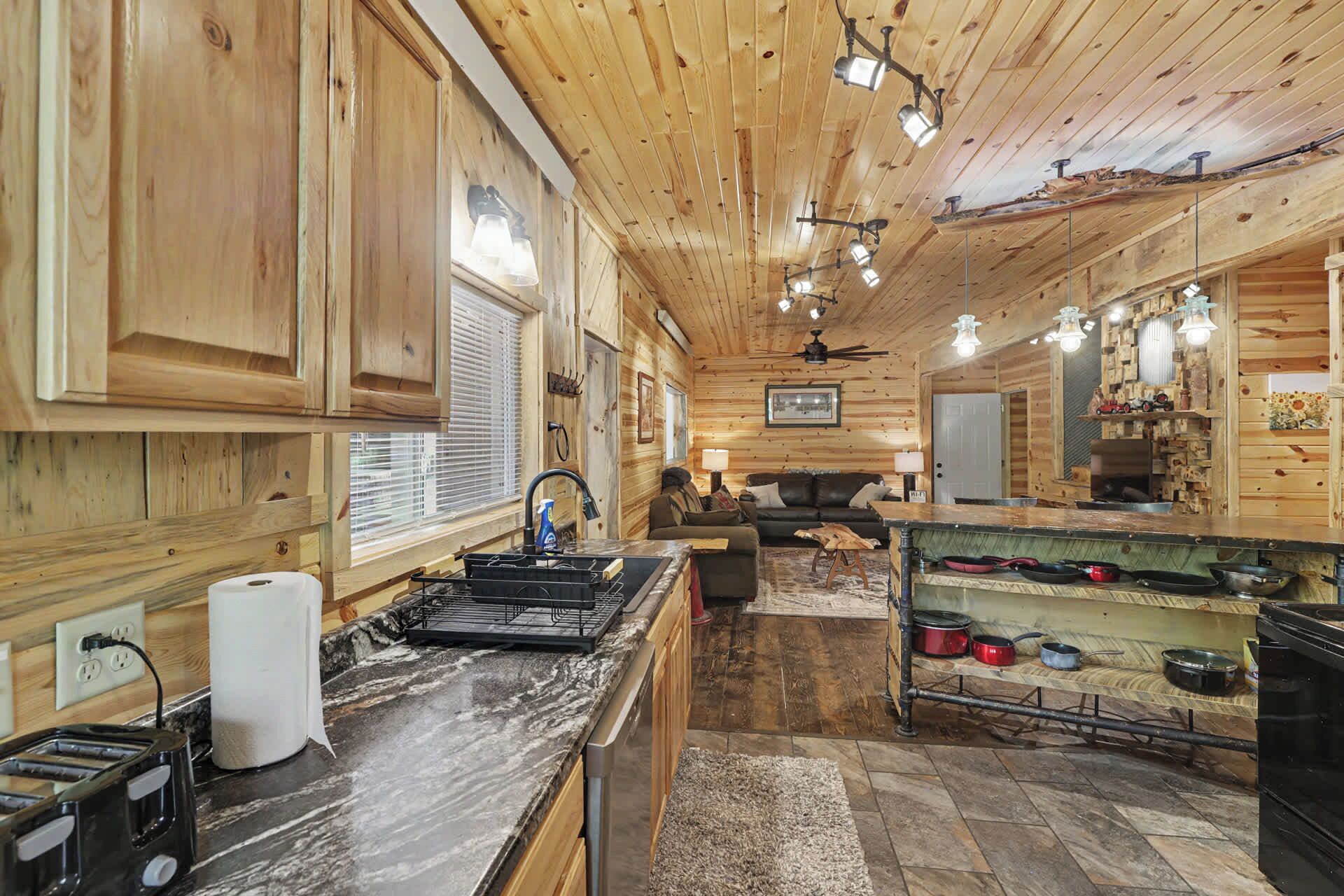 A rustic cabin interior with wooden walls, a kitchen area with a stove, a dining table, and a sofa.