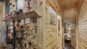 Un interior de madera con una pared de leña apilada, una cama con cabecera de madera y un pasillo que conduce a otra habitación.