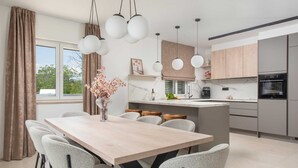 Eine moderne Küche mit Essbereich, ausgestattet mit einem Holztisch, grauen Stühlen, Pendelleuchten und Blick ins Freie.
