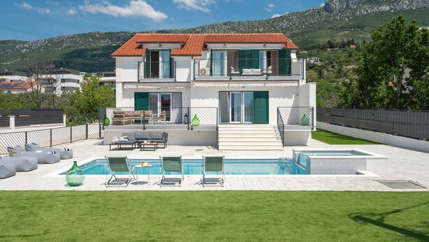 Ein zweistöckiges Haus mit Swimmingpool, grünen Fensterläden und Blick auf eine Berglandschaft.