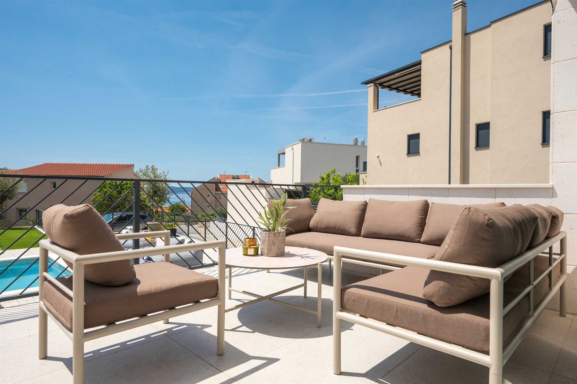 A balcony with a sofa and chairs, a small table, and a view of a swimming pool and buildings.