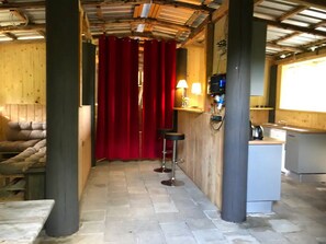 A narrow hallway with a red curtain, wooden walls, a bar area with stools, and a kitchenette. - Sleeping in the Hay—An Adventure Vacation for the Family with a Campfire & a Starry Sky (Burow)